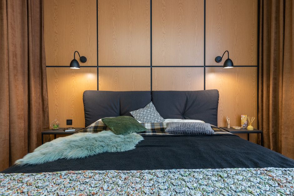 Comfortable big bed with soft cushions and bedside with aroma sticks under shining lamps hanging on wooden wall